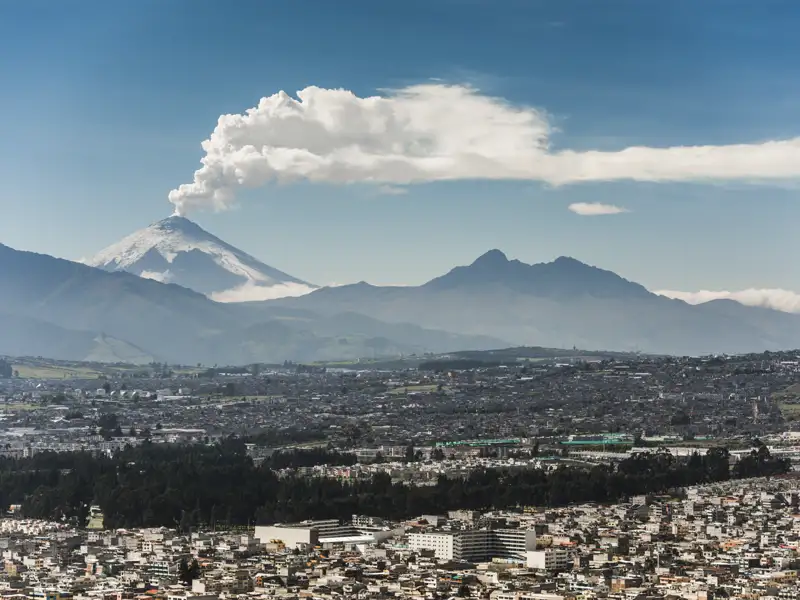 Der Vulkan Cotopaxi mit Rauchfahne über der Stadt.
