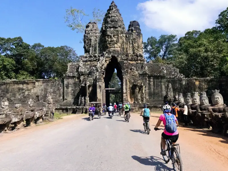 Kambodscha Radreise. Radfahrer auf einer Reise durch Angkor Thom, passieren das Südtor mit den charakteristischen Gesichtern und den steinernen Wächterfiguren.