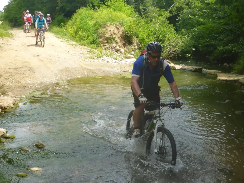 Mountainbiker durchfährt einen Fluss auf einer Radtour.