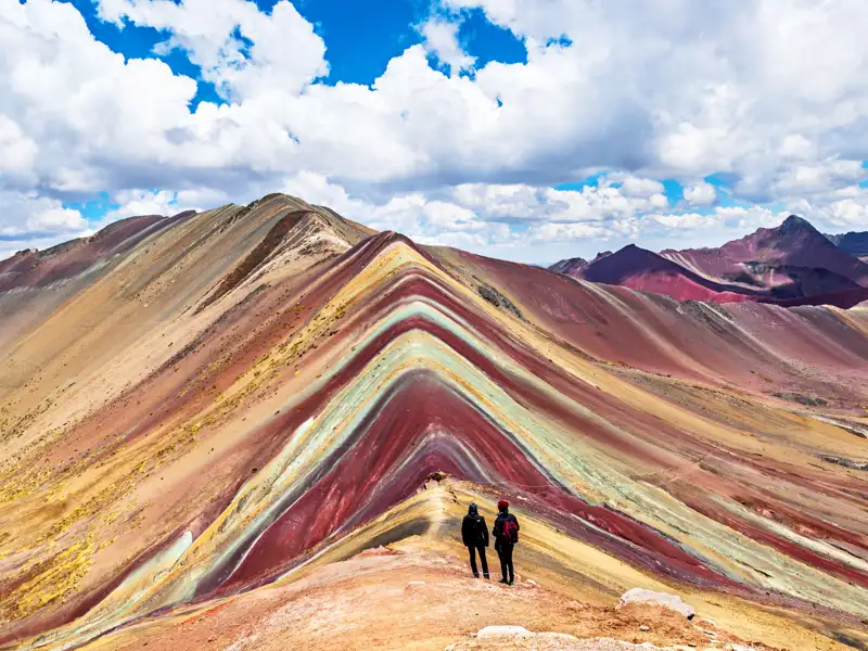 Zwei Wanderer auf dem Vinicunca, auch bekannt als Regenbogenberg, bewundern die vielfarbigen Gesteinsschichten.