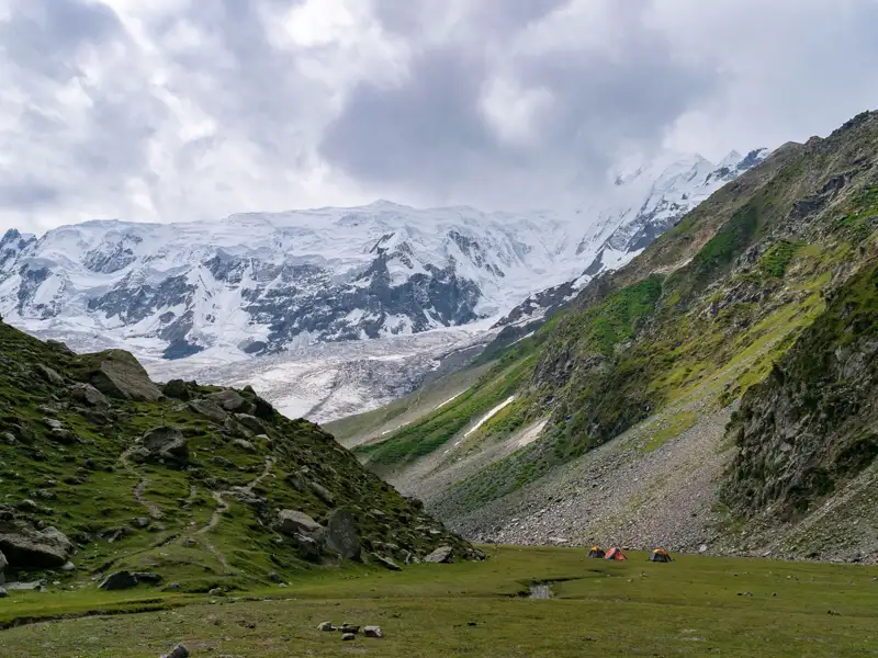 Basislager mit Zelten inmitten einer Hochgebirgslandschaft mit Gletscher und schneebedecktem Berg.