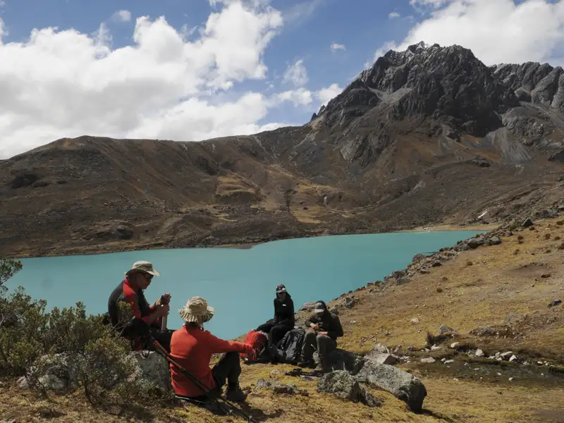 Wanderer pausieren am Ufer eines türkisfarbenen Bergsees inmitten einer bergigen Landschaft.