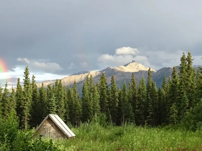 Hütte am Waldrand mit Blick auf die Berge und einen Regenbogen.