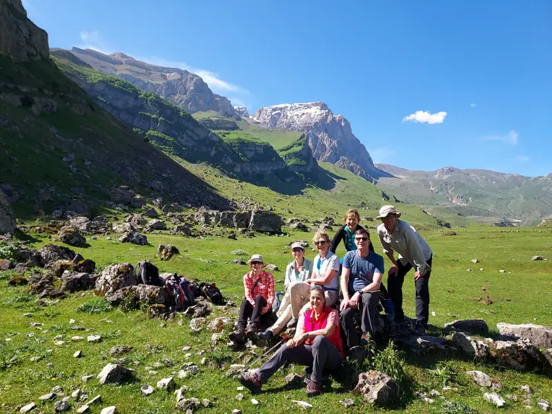 Wandergruppe pausiert im grünen Tal mit Blick auf einen schneebedeckten Berg.