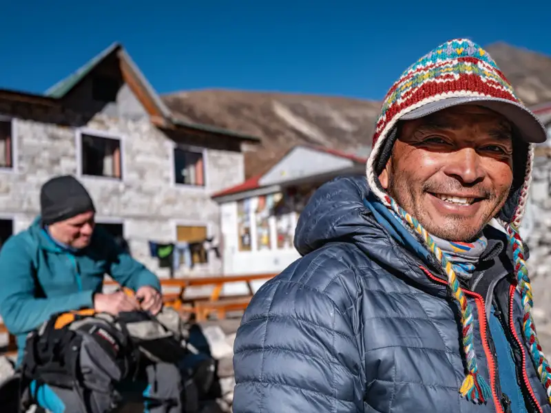 Lächelnder Bergführer während einer Trekkingtour in den Bergen. Im Hintergrund eine Berghütte.