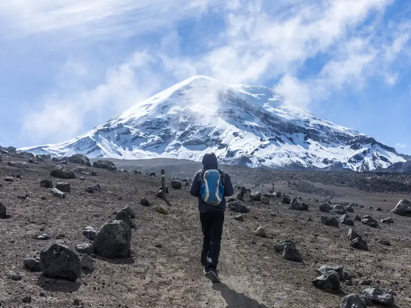 Wanderer auf einem felsigen Pfad mit Blick auf einen schneebedeckten Vulkan.