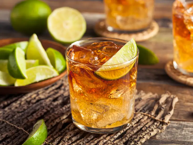 Glas mit einem braunen Getränk, Eiswürfeln und Limettenscheiben.