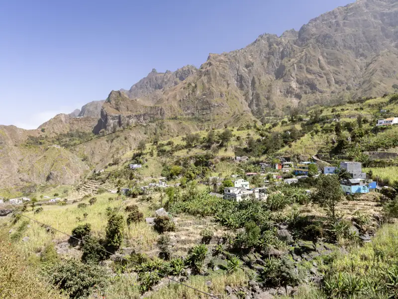 Bergdorf mit Terrassenfeldern und steilen Hängen im Hintergrund.
