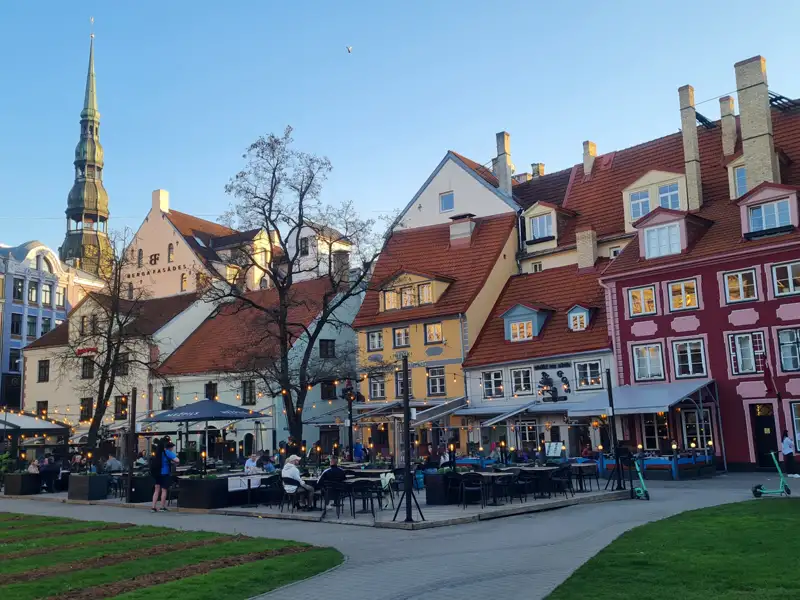 Historische Altstadt von Riga mit Restaurant im Vordergrund und der St. Petri Kirche im Hintergrund.