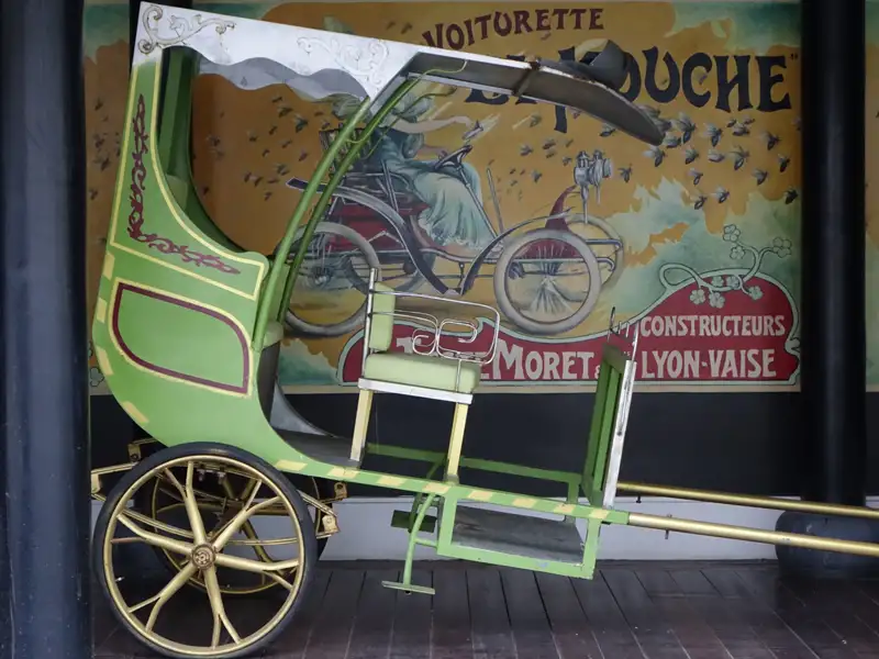 Historische Voiturette vor Werbeplakat von Moret & Lyon-Vaise.