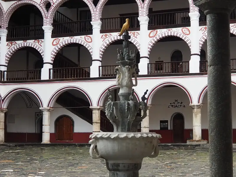 Brunnen im Innenhof eines Klosters mit umliegenden Arkaden und Balkonen.