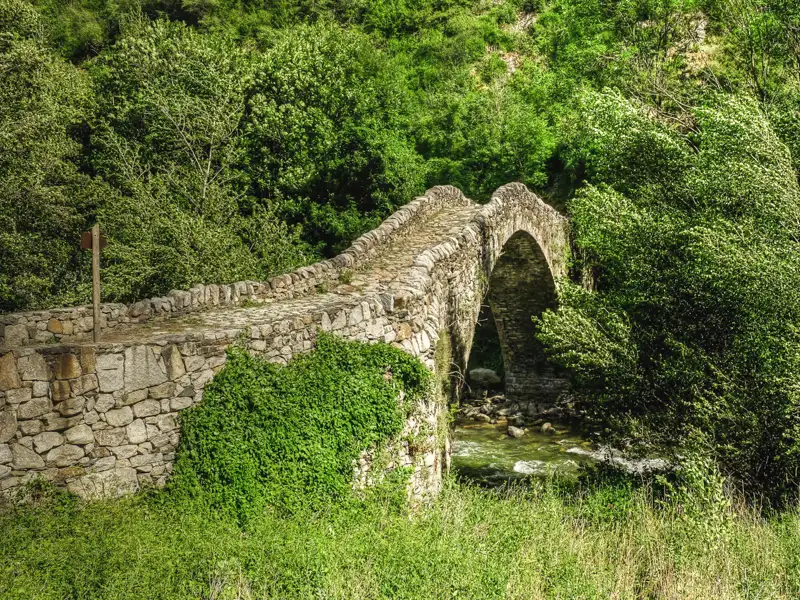 Historische Steinbrücke über einen Fluss inmitten grüner Natur.