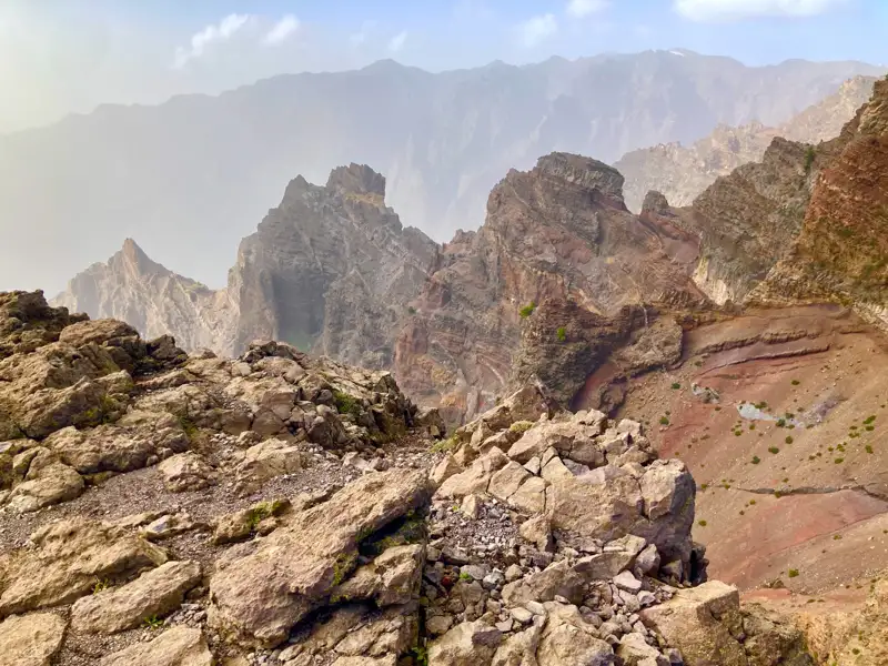 Felsige Berglandschaft mit unterschiedlichen Gesteinsformationen und Bergketten im Hintergrund.