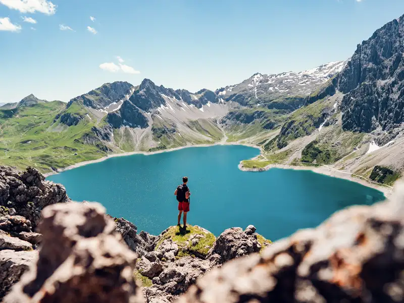 Wanderer mit Blick auf einen türkisblauen Bergsee in den Alpen.