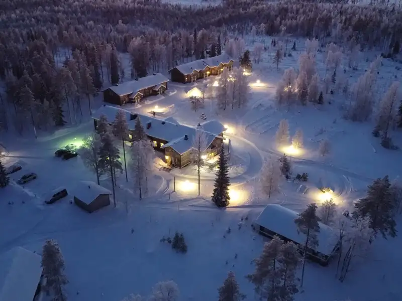Luftaufnahme der Ferienanlage im Schnee, beleuchtet in der Dämmerung.