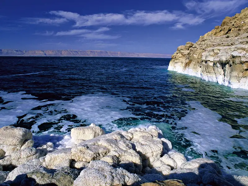 Salzverkrustete Felsen und das tiefblaue Wasser des Toten Meeres.
