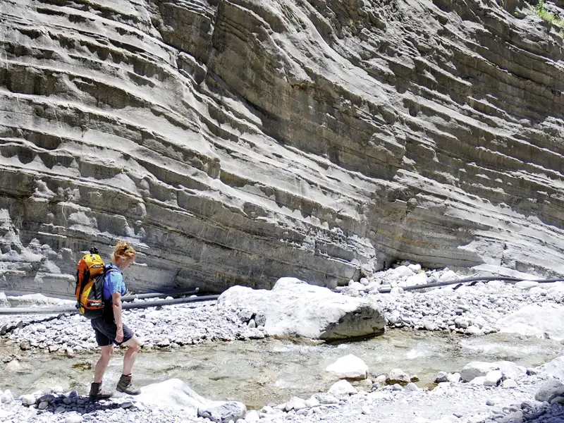 Wanderer durchquert einen Flussbett in einer felsigen Schlucht.