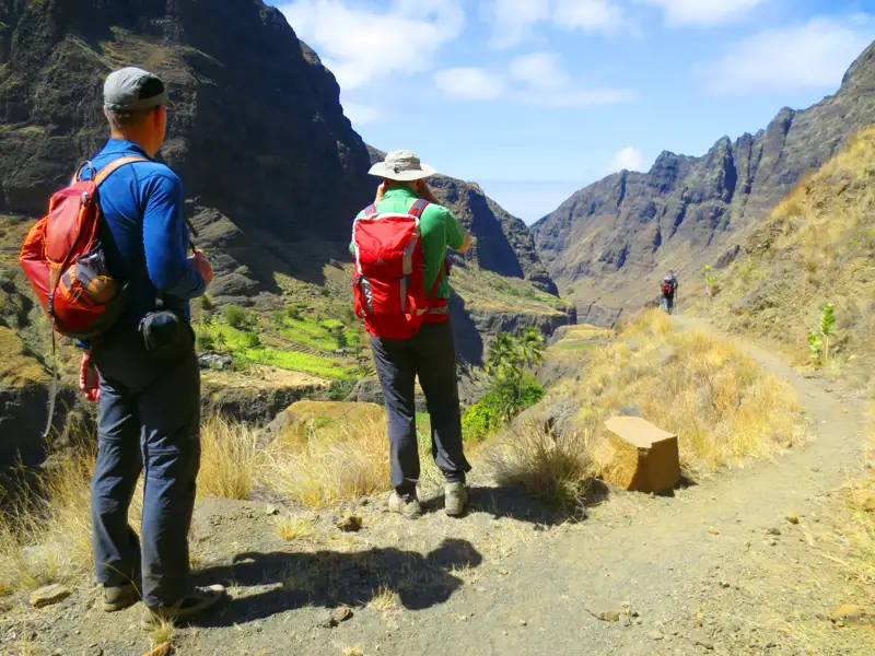 Wanderer auf einem Bergpfad mit Blick auf ein tiefes Tal und landwirtschaftliche Terrassen.