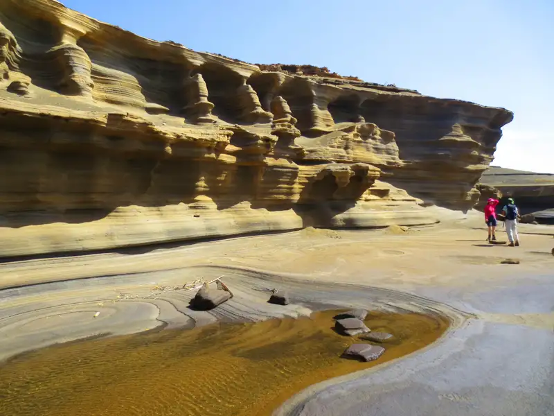 Wanderer erkunden eine Landschaft mit erodierten Felsformationen und einem kleinen Wasserlauf, der durch die Erosion entstanden ist.