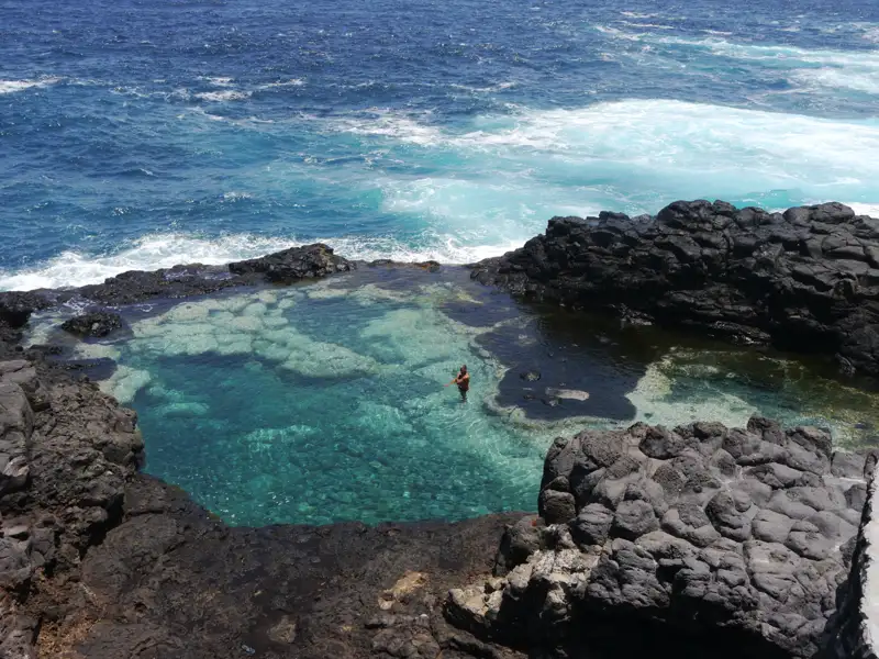 Person schwimmt in einem natürlichen Meerwasserbecken an der Küste.