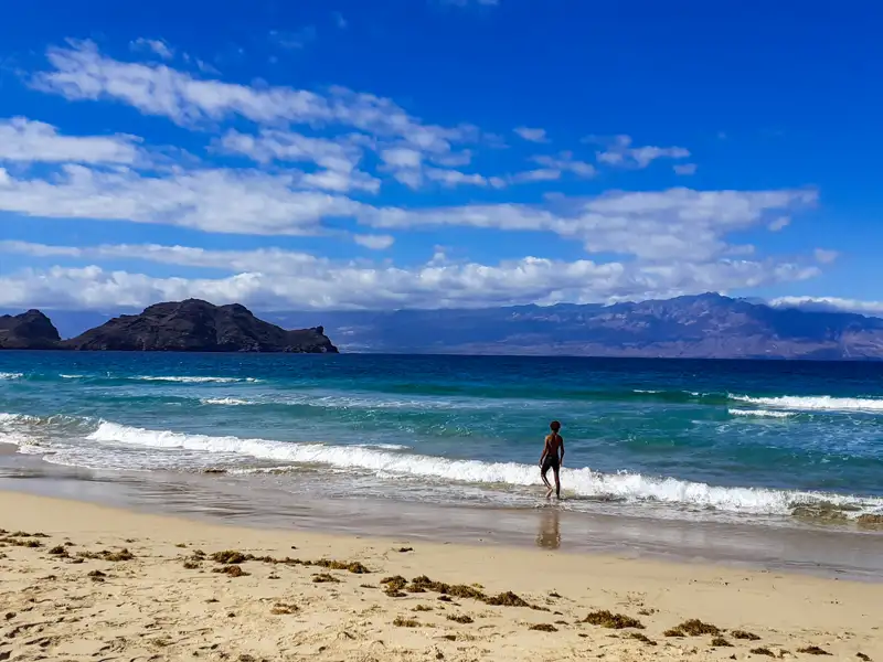 Strandansicht mit einer Person im Wasser, Inseln und Bergen im Hintergrund.