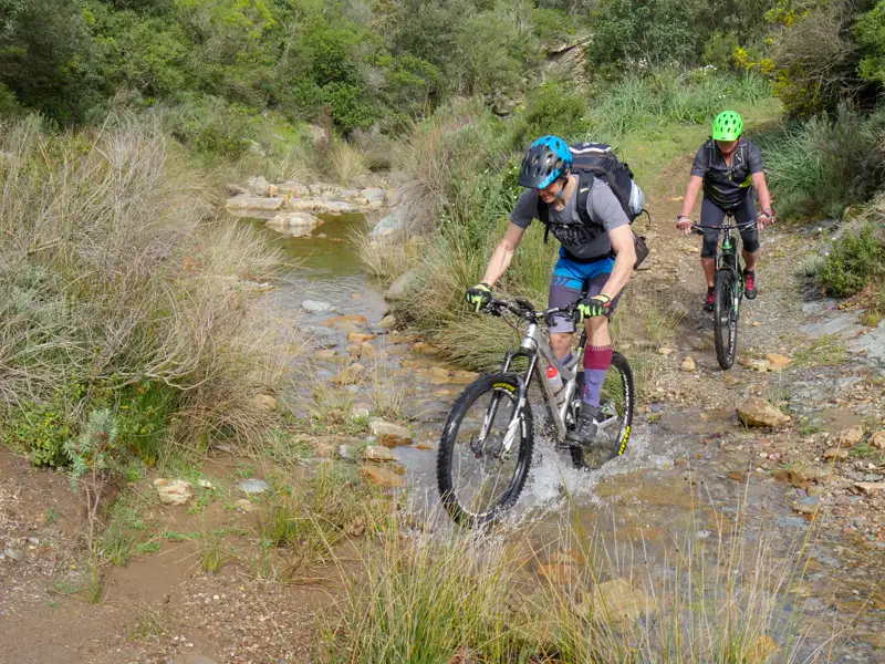 Zwei Mountainbiker durchqueren einen Bach während ihrer Tour.