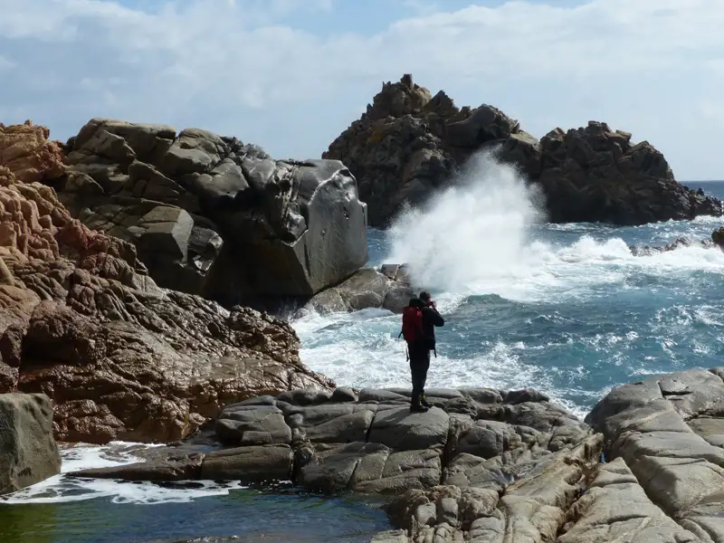 Wanderer fotografiert Brandung an felsiger Küste.