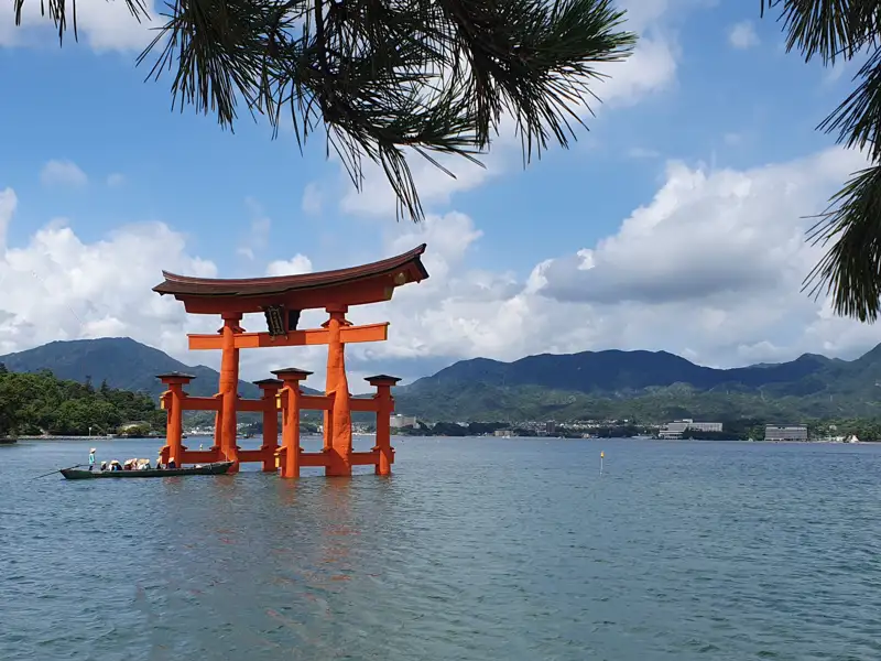 Das berühmte rote Torii des Itsukushima-Schreins, das im Wasser steht, mit Bergen im Hintergrund.