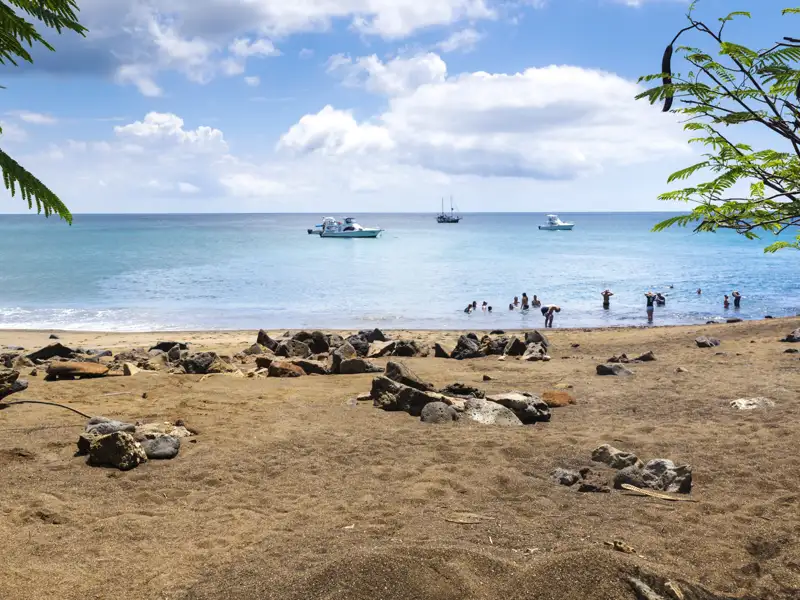 Strandansicht mit Booten und Menschen im Wasser.