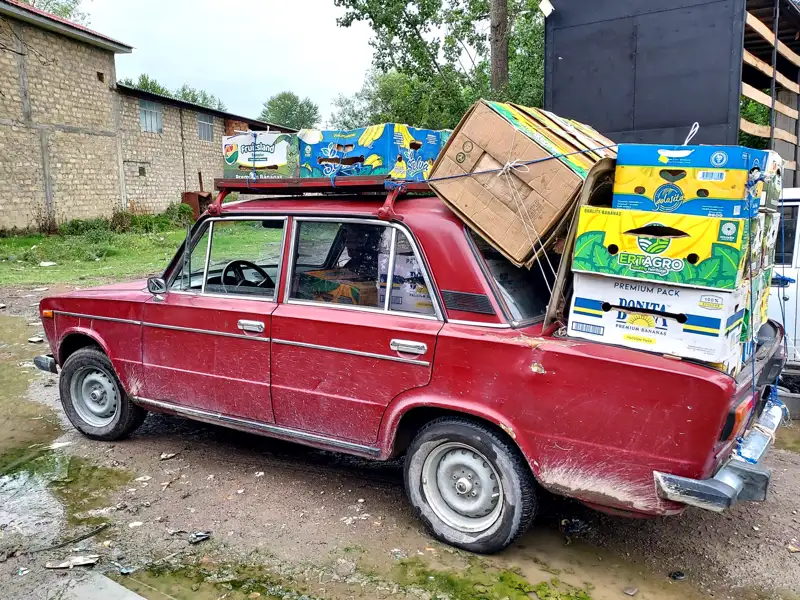 Rotes Auto transportiert Obstkisten auf dem Dach.