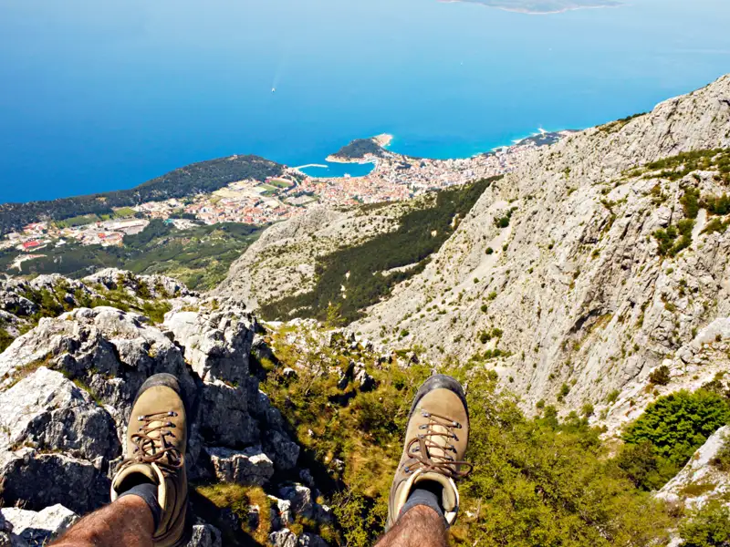 Blick von den Wanderschuhen eines Wanderers auf die Küste und eine Stadt von einem Berggipfel aus.