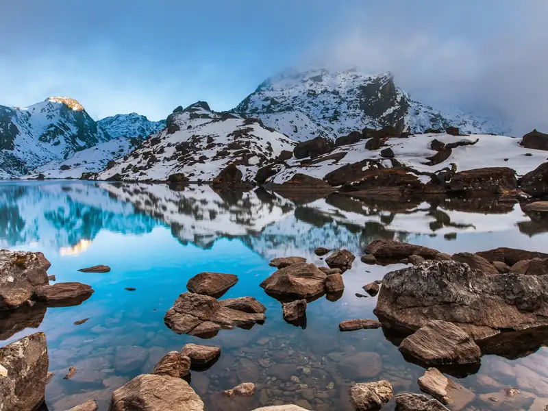 Ruhiger Bergsee mit Spiegelung der umliegenden schneebedeckten Berglandschaft.