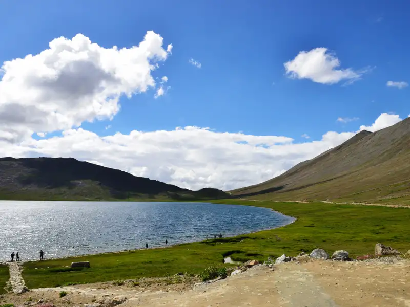 Panoramablick auf einen Bergsee mit umliegenden Bergen und grünem Ufer.