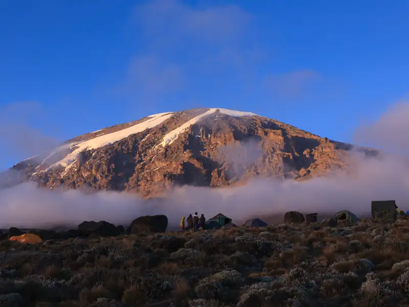Basislager am Fuße eines schneebedeckten Berges. Wanderer bereiten sich vermutlich auf eine Bergtour vor.