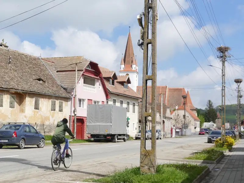Traditionelle Häuser und Kirche in einem Dorf mit Storchennestern auf Strommasten.