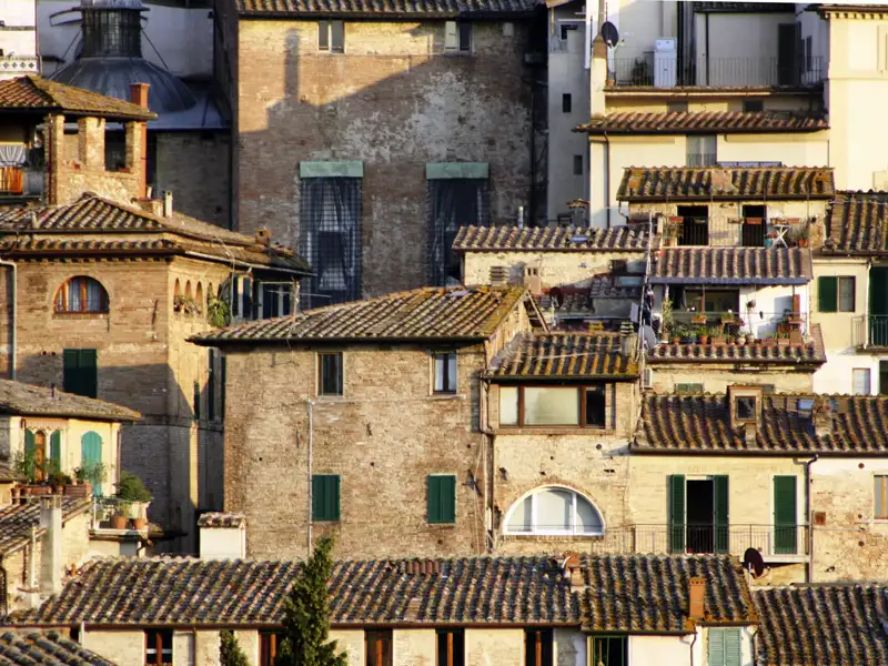 Dicht aneinander gereihte Gebäude mit Ziegeldächern in einer italienischen Stadt.