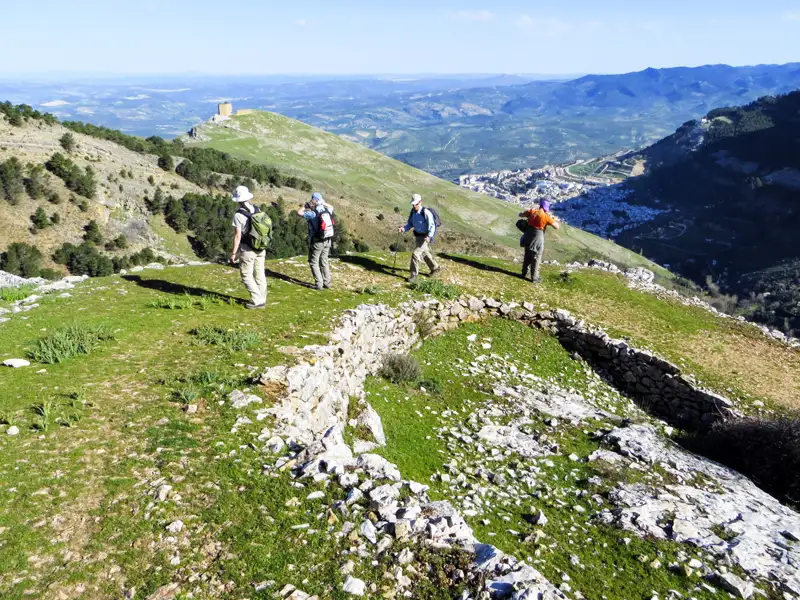 Wanderer auf einem Bergweg mit Blick auf eine Burgruine und die Landschaft.