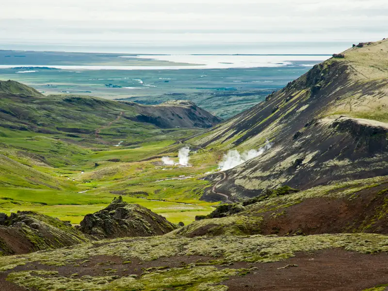 Geothermische Landschaft in Island mit Dampfquellen und Seeblick.