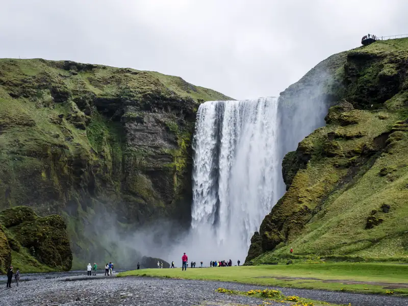 Der imposante Skógafoss Wasserfall in Island mit Besuchern im Vordergrund.