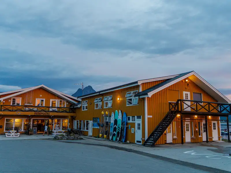 Die Unterkunft des Reiseziels bei Dämmerung. Das gelbe Gebäude mit Rezeption und Wassersportmöglichkeiten.