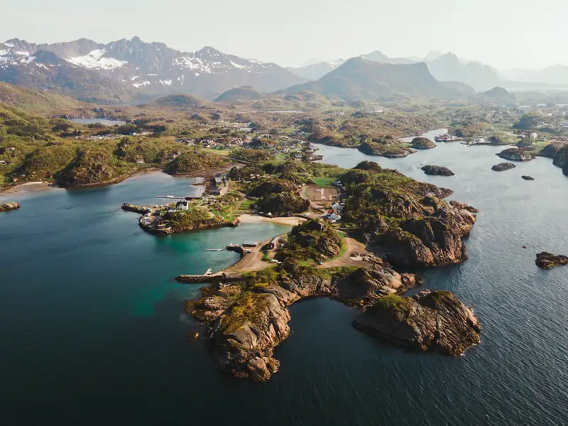 Luftaufnahme der Küste mit felsigen Inseln, einem kleinen Dorf und Bergen im Hintergrund.
