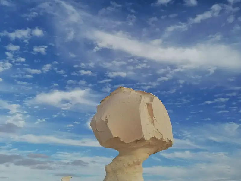 Eine ungewöhnliche Felsformation, die an einen Pilz erinnert, vor einem blauen Himmel mit weißen Wolken.