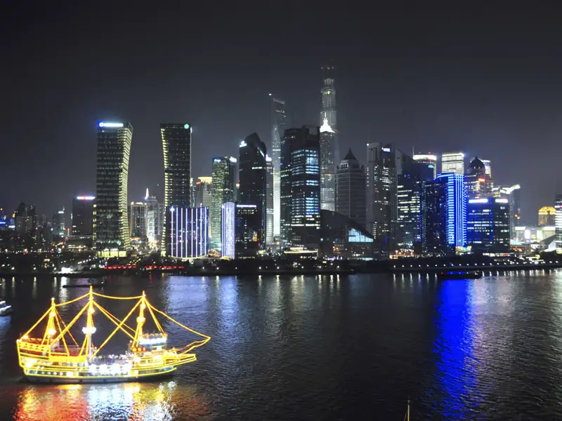Nachtsicht auf die Skyline von Shanghai mit einem beleuchteten Schiff auf dem Fluss.