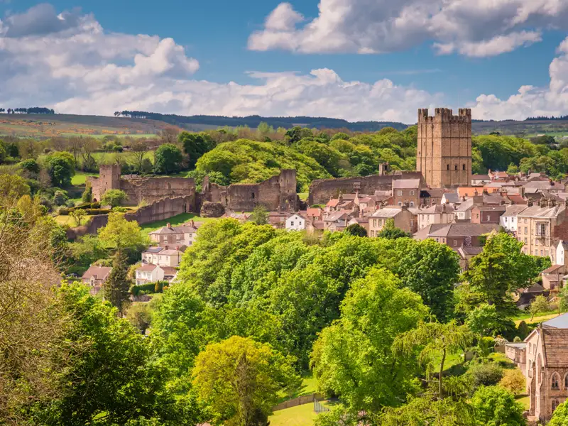 Panoramablick auf Richmond mit der imposanten Burg und den Überresten der Stadtmauer, umgeben von grünen Bäumen und Häusern.