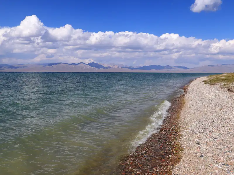Blick auf den See mit Wellen und Bergen im Hintergrund.