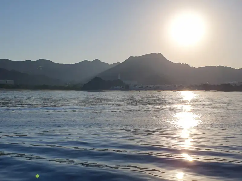 Sonnenuntergang über dem Meer mit Bergen und Küstenlinie im Hintergrund.