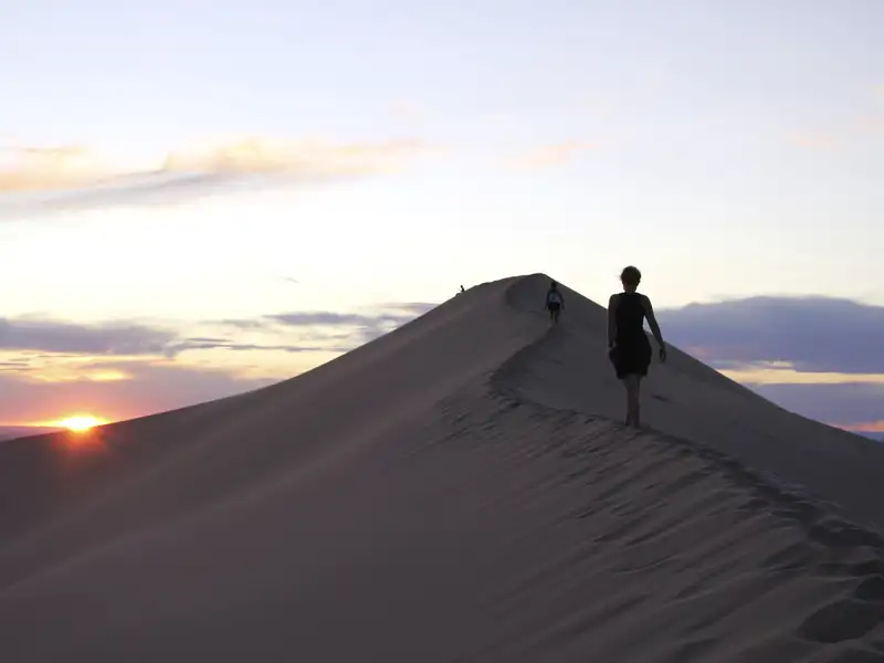 Silhouetten von Wanderern auf einer Sanddüne im Abendlicht.
