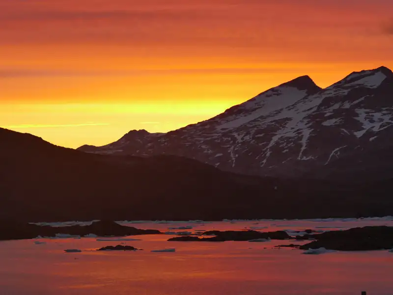Sonnenuntergang über schneebedeckten Bergen und eisbedecktem Wasser.