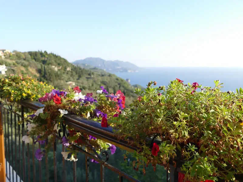 Balkon mit Blumen und Blick auf das Meer und die Hügel.
