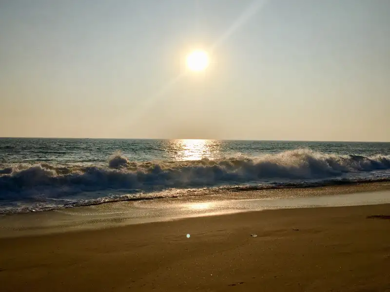 Sonnenuntergang über dem Meer mit Wellen, die am Strand brechen.